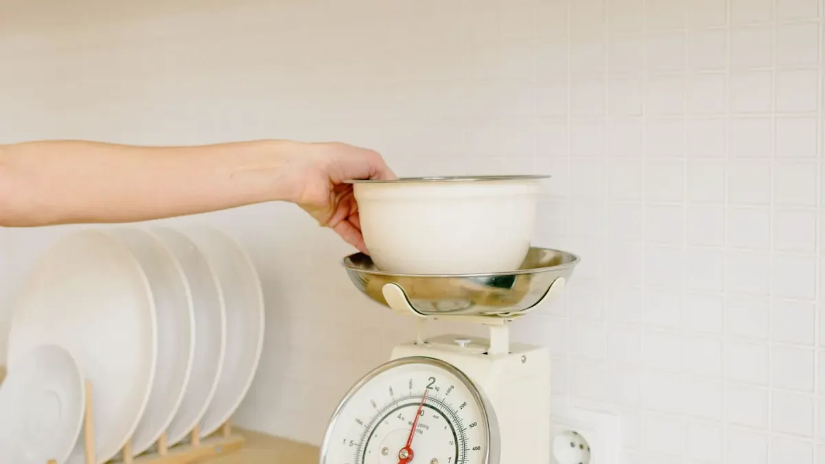 A dog owner scooping a powder supplement into a stainless steel food bowl