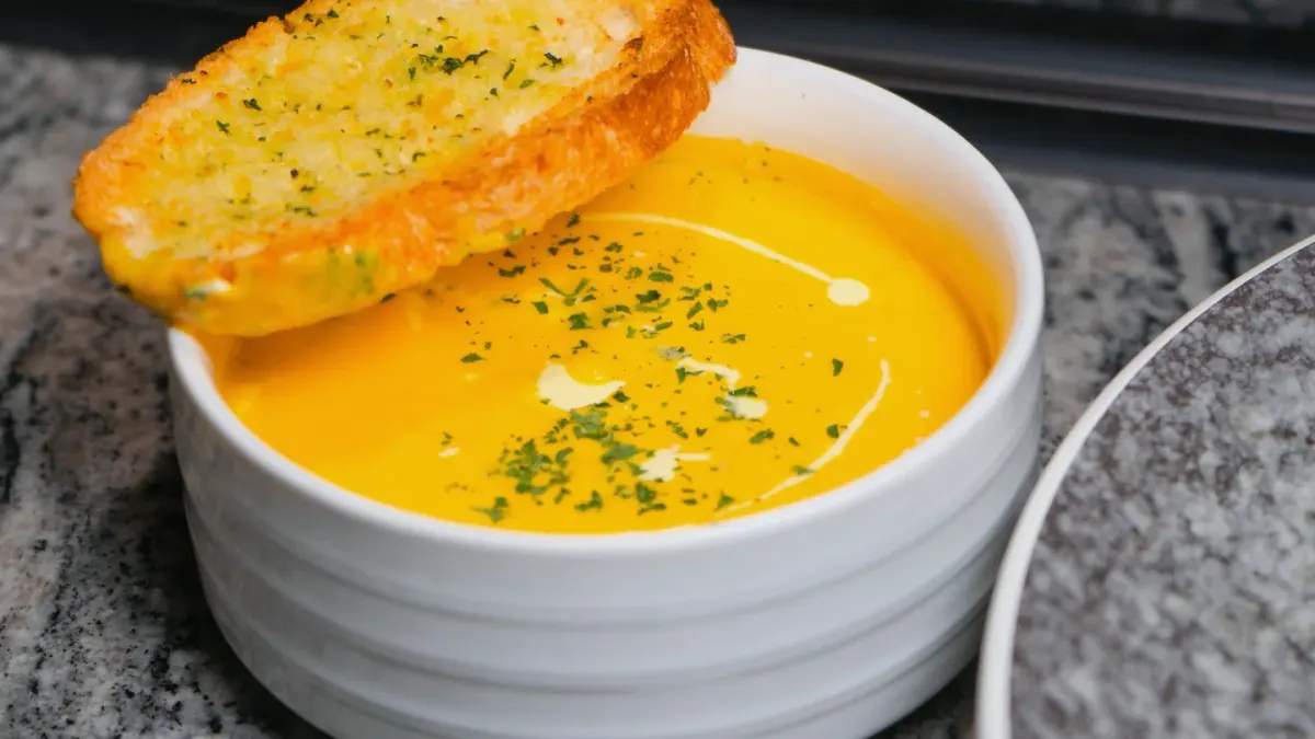 An open can of plain pumpkin puree beside a stainless dog bowl on a kitchen counter