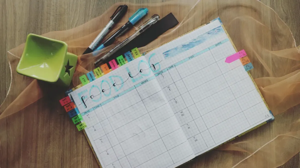 An owner writing notes in a small notebook next to a dog's food bowl